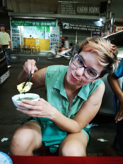 gilda tasting Banh Can with sticks